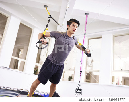 young asian man exercising in gym using fitness straps. 86461751