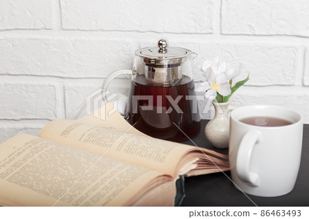 Morning tea. An open old book on the kitchen table and a cup of tea. Leisure reading in a cozy loft-style room 86463493