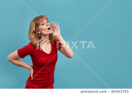Young woman put her hand to face and shout to someone isolated on blue background. Copy, empty space for text 86463765