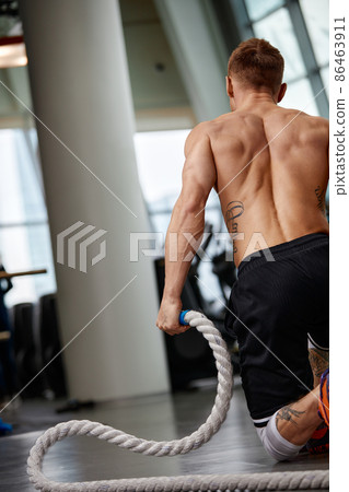 Rear view of Attractive young fit and toned sportswoman working out with battle ropes. Motion blur Rear view of Attractive young fit and toned sportswoman working out with battle ropes. Motion blur 86463911