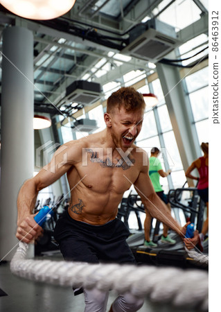 Front view of Attractive young fit and toned sportswoman working out with battle ropes. Motion blur Front view of Attractive young fit and toned sportswoman working out with battle ropes. Motion blur 86463912