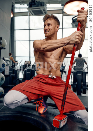 Man fitness training with large and heavy tire hits hammer. Concept workout, cross strength Man fitness training with large and heavy tire hits hammer. Concept workout, cross strength 86463913