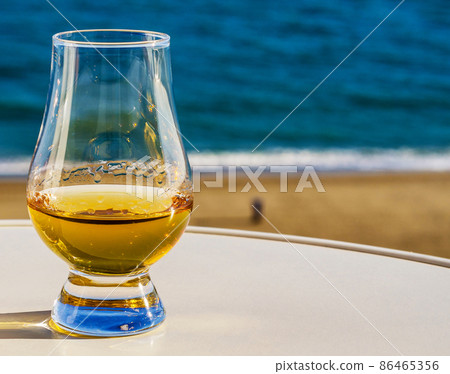 Exclusive single malt whiskey in a tasting glass with a beautiful view of the sea on a sunny day 86465356