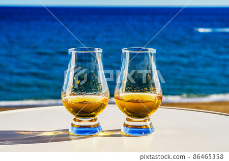 Exclusive single malt whiskey in a tasting glass with a beautiful view of the sea on a sunny day 86465358