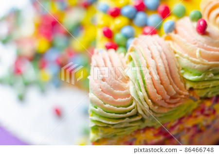 Madeira sponge coated with yellow colour frosting, layered with plum and raspberry jam, filled and topped with multicolour chocolate nibs and decorated with multicolour frostings and sugar decorations 86466748