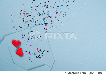 Valentine's day festive background. Blue envelope with red hearts and multicolored confetti around on pastel blue background with copy space. Flat lay, top view 86466885