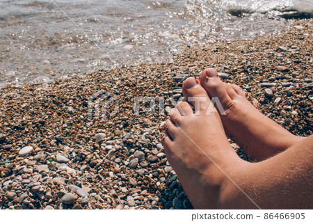 Unrecognisable child sitting on the beach near water, children's legs against sea shore as summer vacation background with copy space Unrecognisable child sitting on the beach near water, children's legs against sea shore as summer vacation background with copy space 86466905