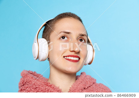 Happy pretty girl, student with short hair wearing pink hoodie in headphones isolated on blue background. Concept of emotions, music Happy pretty girl, student with short hair wearing pink hoodie in headphones isolated on blue background. Concept of emotions, music 86466909