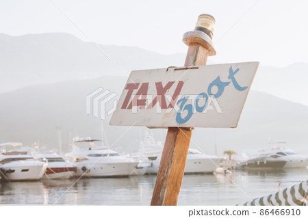 Taxi boat signboard in marina with defocused sailboats as background. Tourist attraction and sea tourist transport. Sea walks during summer vacations in Montenegro, Italy, Spain, Croatia or France Taxi boat signboard in marina with defocused sailboats as background. Tourist attraction and sea tourist transport. Sea walks during summer vacations in Montenegro, Italy, Spain, Croatia or France 86466910