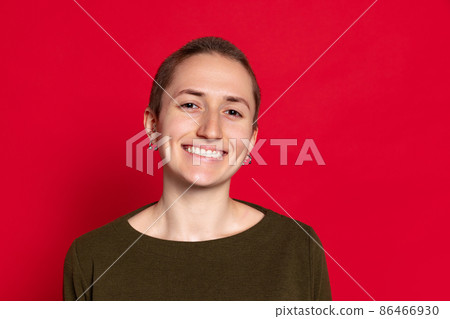 Portrait of young smiling woman, student with short hair in dark sweater isolated on red background. Concept of emotions, studying, ad Portrait of young smiling woman, student with short hair in dark sweater isolated on red background. Concept of emotions, studying, ad 86466930