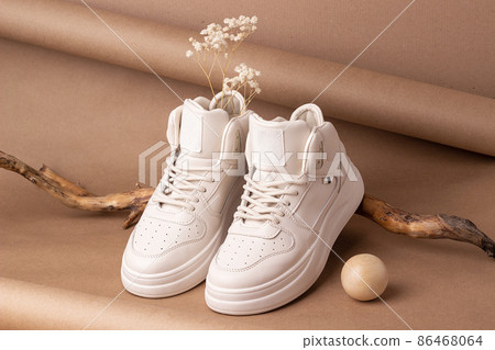 Eco leather shoes. A pair of beige sneakers with dry flowers on the wood, brown background. Casual sport lifestyle concept 86468064
