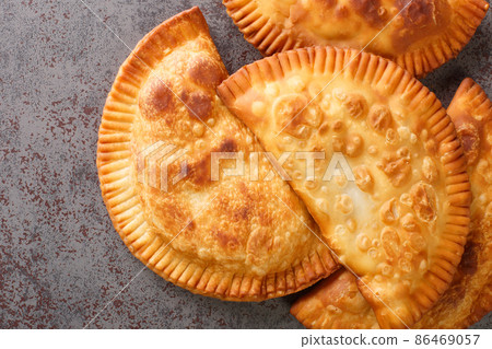 Chebureki is a deep-fried turnover with a filling of ground or minced meat and onions close up in the table. Horizontal top view Chebureki is a deep-fried turnover with a filling of ground or minced meat and onions close up in the table. Horizontal top view 86469057