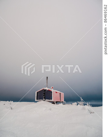 Vertical minimalistic background with of lonely red cabin in winter. Dubladom on the mountain Volodyanaya Kandalaksha, Murmansk region in Russia. 86469162