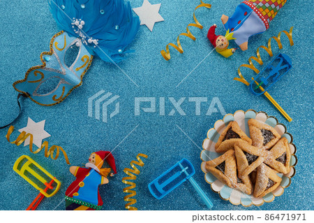 Jewish holiday Purim background with hamantaschen or hamans ears cookies, carnival mask and noisemaker Jewish holiday Purim background with hamantaschen or hamans ears cookies, carnival mask and noisemaker 86471971