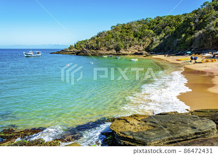 Paradise beach with colorful transparent waters surrounded by stones and vegetation Paradise beach with colorful transparent waters surrounded by stones and vegetation 86472431