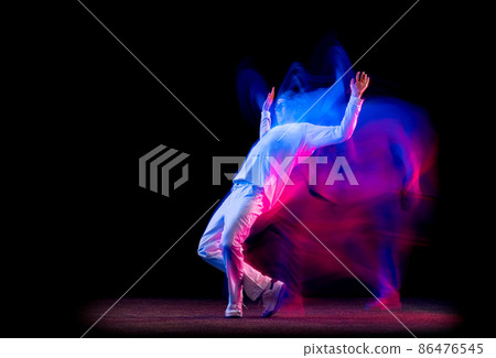 Dynamic portrait of male hip-hop dancer dancing isolated on dark background in mixed neon light. Youth culture, hip-hop, movement, style and fashion, action. 86476545