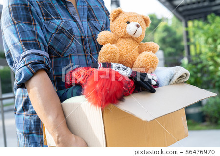 Holding clothing donation box with used clothes and doll at home to support help for poor people in the world. 86476970