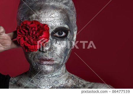 Portrait of a Beautiful young woman with a clay mask on her face, which is covered with silver paint 86477539
