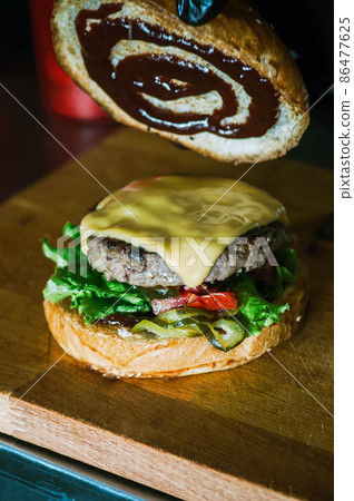 Rich cheeseburger in making, fluffy buns, beef burger meat, lettuce, bbq sauce and cheese. 86477625