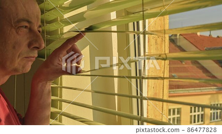 Midlle age man looking through a jalousie. Themes curiousity, surveillance or eyesight 86477828