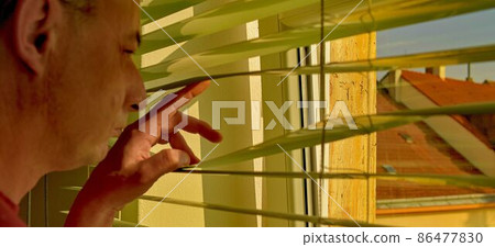 Midlle age man looking through a jalousie. Themes curiousity, surveillance or eyesight 86477830