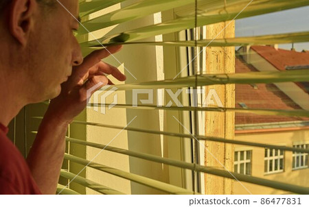 Midlle age man looking through a jalousie. Themes curiousity, surveillance or eyesight Midlle age man looking through a jalousie. Themes curiousity, surveillance or eyesight 86477831