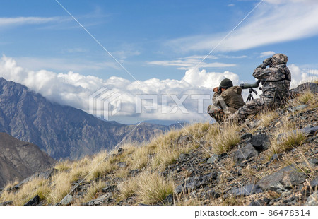 Shooters in mountain gear on the slope are watching the situation through binoculars. Shooters in mountain gear on the slope are watching the situation through binoculars. 86478314