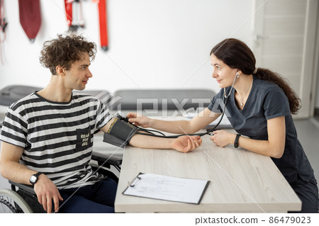 Medical worker measures the pressure of a young man in a wheelchair 86479023