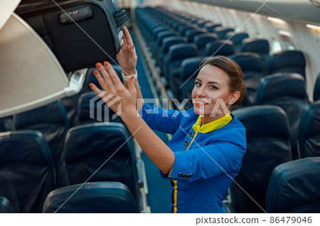 Stewardess putting travel bag in overhead luggage shelf in airplane Stewardess putting travel bag in overhead luggage shelf in airplane 86479046