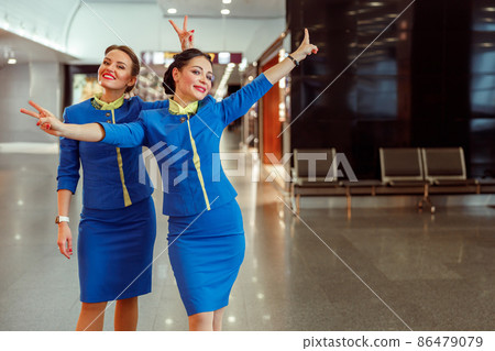 Cheerful women stewardesses showing victory gesture at airport Cheerful women stewardesses showing victory gesture at airport 86479079