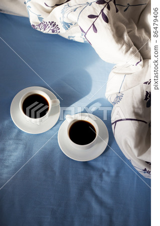Two white cups of coffee are in bed, sunny morning Two white cups of coffee are in bed, sunny morning 86479406