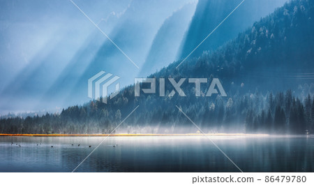 Mountains in bright sunbeams and foggy lake at sunny morning in summer. Dolomites, Italy 86479780