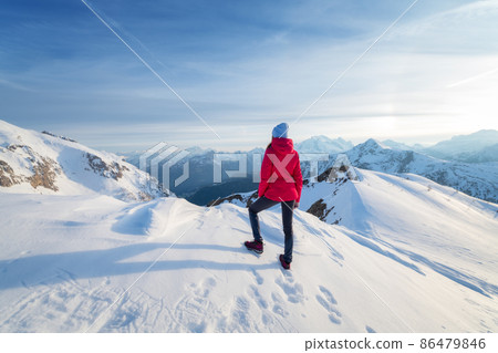 Young woman in red jacket in snowy mountains at sunset in winter Young woman in red jacket in snowy mountains at sunset in winter 86479846