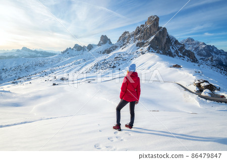 Young woman in red jacket in snowy mountains at sunset in winter 86479847