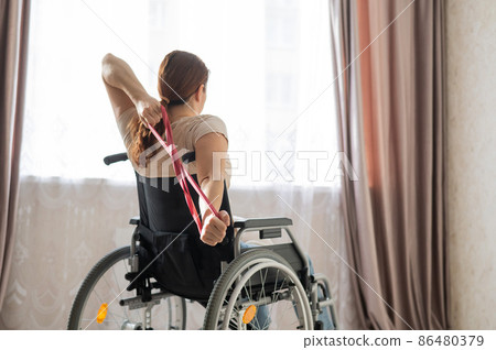Caucasian woman in a wheelchair doing exercises with the help of fitness rubber bands. Caucasian woman in a wheelchair doing exercises with the help of fitness rubber bands. 86480379