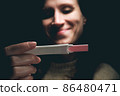 A woman in a dark room looks at the result of a pregnancy test and smiles. 86480471