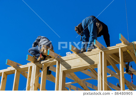 Worker in holding plank installing it on household construction using air hammer in nailing wooden beams Worker in holding plank installing it on household construction using air hammer in nailing wooden beams 86480905