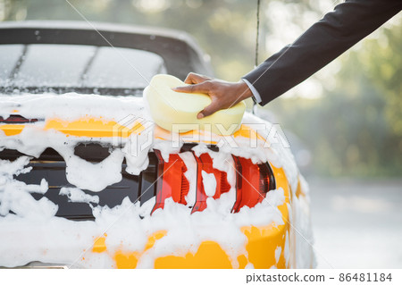 Closeup cropped image of hand of young African man with yellow sponge washing Back lights headlight 86481184