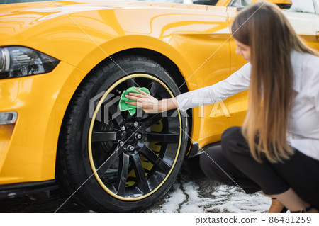 Business woman wearing on a white shirt and black trousers cleaning a wheel, car rims 86481259