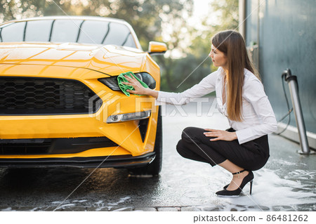 Cheerful business woman washing and wiping modern sport yellow car headlight Cheerful business woman washing and wiping modern sport yellow car headlight 86481262