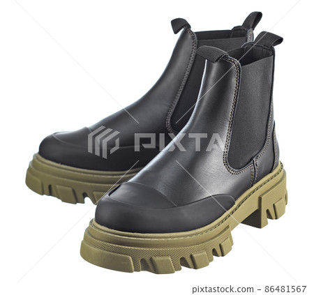 Beautiful pair of high black demi-season leather boots with an elastic band with a massive dark-green sole, isolated on a white background. 86481567