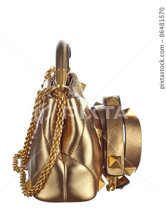 Handbag made of genuine leather in gold color, decorated with chains and rivets in the shape of pyramids, with a metal clasp, isolated on a white background. Side view. Expensive women's accessories. Handbag made of genuine leather in gold color, decorated with chains and rivets in the shape of pyramids, with a metal clasp, isolated on a white background. Side view. Expensive women's accessories. 86481570