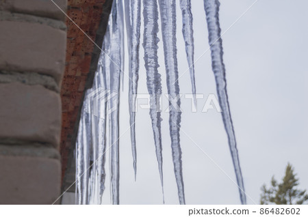 Icicles of ice hang from the roof of the building. Melting snow on the roof of the house. Spring. Selective focus 86482602