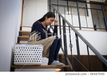 Image of a housewife tired of housework ・ A woman worried in front of a laundry basket on the stairs 86487040