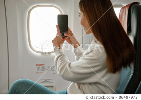 Young woman taking photo with smartphone in airplane Young woman taking photo with smartphone in airplane 86487972