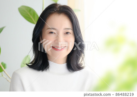 A beautiful Japanese (Asian) woman smiling in a bright room up. There is a copy space on the right. There is a blur in front. 86488219