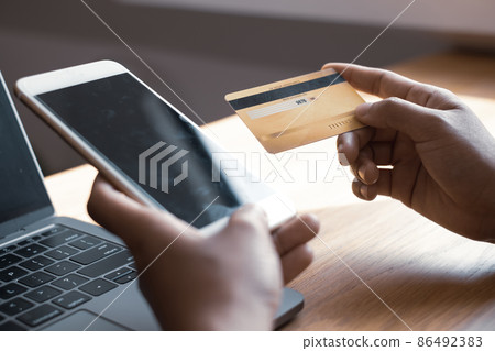 The businesswoman's hand is holding a credit card and using a smartphone for online shopping and internet payment The businesswoman's hand is holding a credit card and using a smartphone for online shopping and internet payment 86492383
