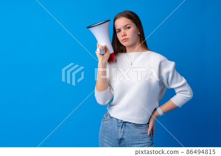 Teen girl making announcement with megaphone at blue studio 86494815