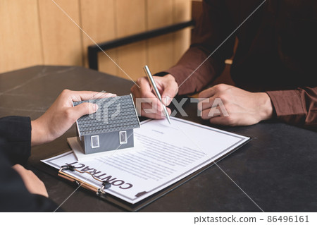A real estate agent with a house model is talking to clients about buying home insurance and having customers sign contracts under the formal contract agreement. Home rental and insurance concept 86496161
