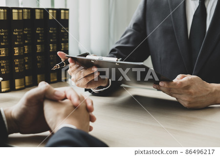 A male lawyer or a judge counseling clients about judicial justice and prosecution with scales, judges gavel, legal documents legal services concept 86496217